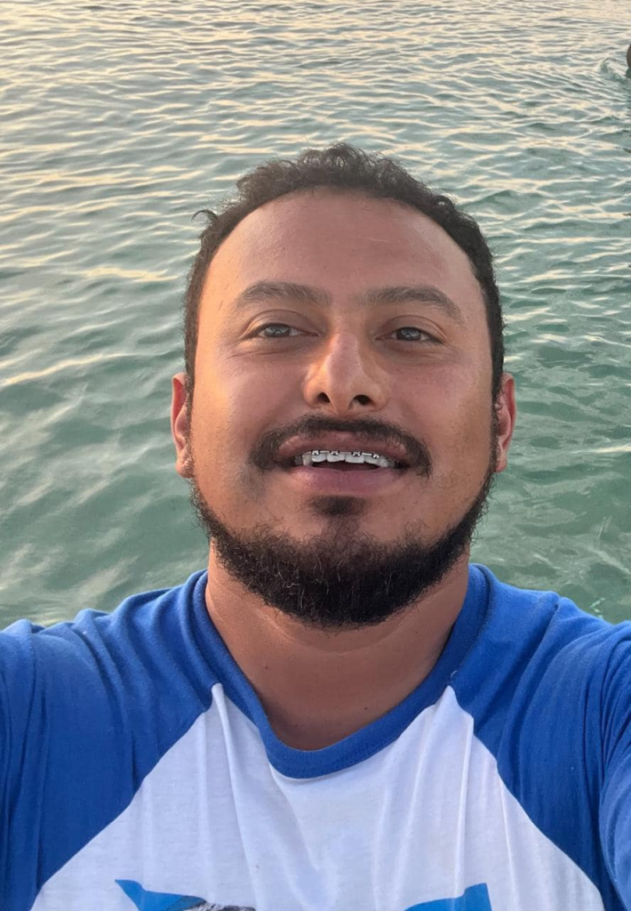 Selfie de Servando Salazar Cano sonriendo mientras está en la playa, con el mar de fondo. Lleva puesta una camiseta azul y blanca.