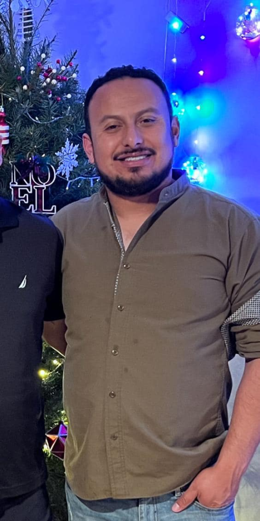 Imagen de Servando Salazar Cano posando frente a un árbol de Navidad decorado. Está sonriendo y vestido con una camisa marrón.